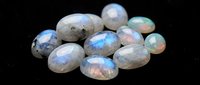 Collection of polished rainbow moonstone gems with iridescent blue flash on black background for jewelry making and gemstone crafts.