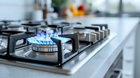 Blue gas flame burning on modern stainless steel stove in contemporary kitchen interior, close up view showing clean burner grate and professional cooking surface.