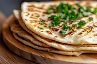 Fresh homemade naan bread stack garnished with chopped herbs on wooden serving board, close up view of traditional Indian flatbread with grilled marks.