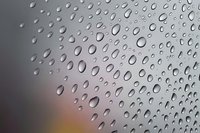 Water drops on glass surface create natural abstract pattern with blurred warm background tones, capturing condensation and pure freshness.