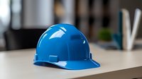 Blue construction hard hat on light surface against blurred office background, workplace safety equipment for industrial and engineering projects.