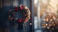 Festive wreath with red poinsettias, pine cones and twinkling lights hanging on dark wooden door, blurred Christmas tree lights in background creating magical atmosphere.