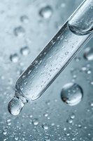 Glass dropper with water drops on light blue surface, macro photography showing transparent liquid and droplet formation in scientific laboratory setting.