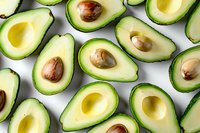 Fresh ripe avocado halves arranged in rows showing creamy yellow flesh and brown pits against white background, overhead view pattern layout for healthy food concept.