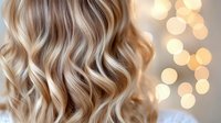 Luxurious blonde wavy hair with soft highlights on blurred bokeh background. Professional hairstyling showcases natural-looking waves and dimensional color technique.