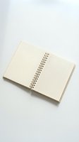 Open spiral-bound notebook with blank cream pages and grid pattern on right side, displayed on white background for stationery and office supplies use.