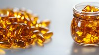 Golden omega-3 fish oil capsules spilling from glass jar on white background. Dietary supplements for heart health and wellness nutrition support.