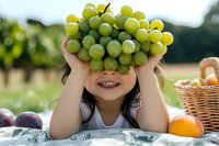 Green grapes cluster held by smiling young girl with dark hair at vineyard picnic, fresh fruit harvest concept for food and agriculture marketing.