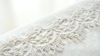Cream linen fabric with delicate lace trim and fringe edge detail, isolated on white background for textile design, fashion, and home decor projects.