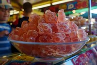 Pink gummy bears piled high in glass bowl at candy store display, soft focus background creates depth with vibrant colors and sweet shop atmosphere.