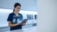 Female healthcare professional analyzing brain scan results on digital tablet in modern medical facility for neurological diagnosis and patient care.