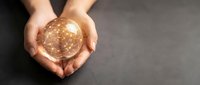 Hands holding glowing golden sphere with light particles on dark background, representing innovation, future technology, energy, and success concepts for business presentations.