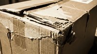 Old worn cardboard boxes with torn edges and damaged corners stacked together showing signs of heavy use and weathering in warm sepia tones.