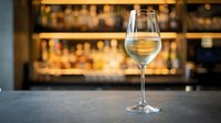 Glass of white wine on bar counter with blurred restaurant background. Elegant stemware for dining, hospitality and beverage service concepts.