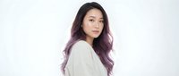 Young Asian woman with long purple ombre hair wearing white sweater looking at camera against clean white background for portrait photography.