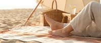 Woman relaxing on sandy beach under tent with picnic basket, enjoying summer vacation and outdoor leisure activities.
