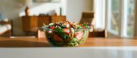 Fresh arugula salad with strawberries, nuts, and greens in a glass bowl on a wooden counter in a bright modern kitchen.