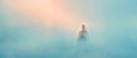 Solitary figure standing in dense fog and mist during early morning or twilight hours, creating an atmospheric and ethereal mood suitable for conceptual and editorial projects.