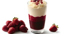 Layered dessert with red berry puree and whipped cream topped with dried cranberries, fresh strawberries arranged beside glass for food photography.