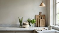 Minimalist kitchen counter with marble surface, fresh herbs, wooden cutting boards, and brass pendant lamp in neutral tones.