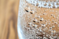 Macro shot of sparkling water bubbles in glass against wooden background, showing transparent spherical formations and natural refraction patterns.