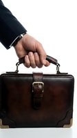 Businessman holding brown leather briefcase with metal buckle and handles against white background, isolated for corporate and professional use.