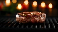 Juicy beef steak grilling on barbecue with bokeh lights in background. Close up of medium rare meat with perfect grill marks and seasonings on dark surface.
