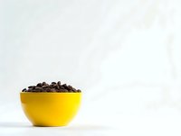 Fresh roasted coffee beans in bright yellow ceramic bowl against white background, minimalist composition for cafe and restaurant marketing.