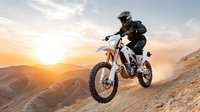 Motocross rider jumping dirt bike on mountain slope during golden sunset with dramatic sky and rugged terrain for extreme sports and adventure content.