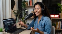 Young Hispanic woman podcaster recording show in home studio with microphone, laptop and on air sign. Content creator broadcasting from cozy workspace.