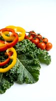 Fresh organic vegetables with kale leaves, colorful bell pepper rings and cherry tomatoes on white background for healthy cooking and nutrition.