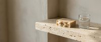 Minimalist bathroom shelf with natural soap bars and glass of water on terrazzo surface against neutral wall backdrop.