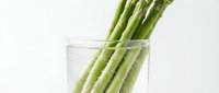 Fresh green asparagus spears in clear glass container on white background. Healthy organic vegetable for cooking and nutrition concepts.