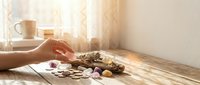 Woman hand reaching for chocolate candies and sweets on wooden table with warm sunlight streaming through window creating cozy atmosphere.