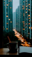 Coffee cup and notebook on windowsill overlooking illuminated city skyscrapers at dusk creating cozy urban workspace atmosphere for productivity and relaxation.
