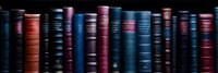 Row of vintage hardcover books with colorful spines in blue, red, and burgundy shades against dark background creates dramatic library atmosphere.