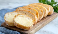 Fresh baguette slices filled with creamy butter spread arranged on wooden cutting board, garnished with herbs against marble background.