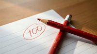 Red pencil with perfect score of 100 circled on lined paper for academic achievement and educational success concepts.