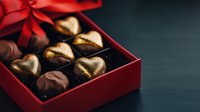 Heart-shaped chocolate pralines with golden glitter in red gift box on dark background. Romantic sweets assortment for special occasions and celebrations.