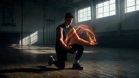 Young athletic African American male basketball player kneeling on wooden court floor in dramatic sunlit gym preparing for training session.