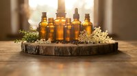 Amber glass bottles with essential oils arranged on rustic wooden tray with dried herbs and flowers in warm natural lighting for aromatherapy wellness.