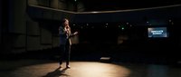 Professional businesswoman presenting on stage in modern conference hall with spotlight and screen for corporate events and public speaking engagements.