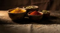 Aromatic spices in wooden bowls on rustic table. Turmeric, paprika, cardamom pods create warm culinary scene for cooking and seasoning recipes.