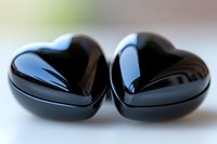 Two glossy black ceramic hearts placed side by side on light surface, showing reflection and smooth texture. Romantic symbol for love and relationship.