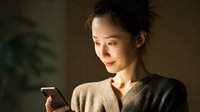 Young Asian woman using smartphone in warm indoor lighting, casual sweater, technology communication lifestyle for social media marketing content.