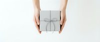 Female hands holding elegant white gift box with silver ribbon bow on clean white background for special occasions and celebrations.