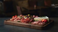 Gourmet charcuterie board with assorted cured meats, cheese, olives and garnishes on wooden serving platter for entertaining and appetizer presentations.