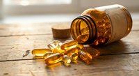 Amber vitamin capsules spilling from brown glass bottle on wooden surface. Health supplement pills for wellness and nutrition support in natural lighting.