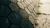 Hexagonal basalt columns meet cracked concrete pavement with moss growth, showing natural weathering and urban decay textures for background and design use.