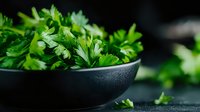 Fresh green parsley leaves in dark bowl on kitchen counter for cooking and culinary preparations.